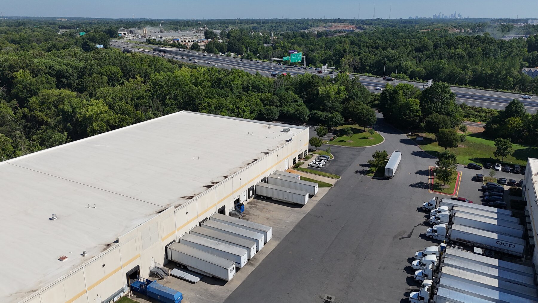 Aerial view of the Rodney Street warehouse showing loading docks, truck staging, highway access, and the Charlotte skyline.